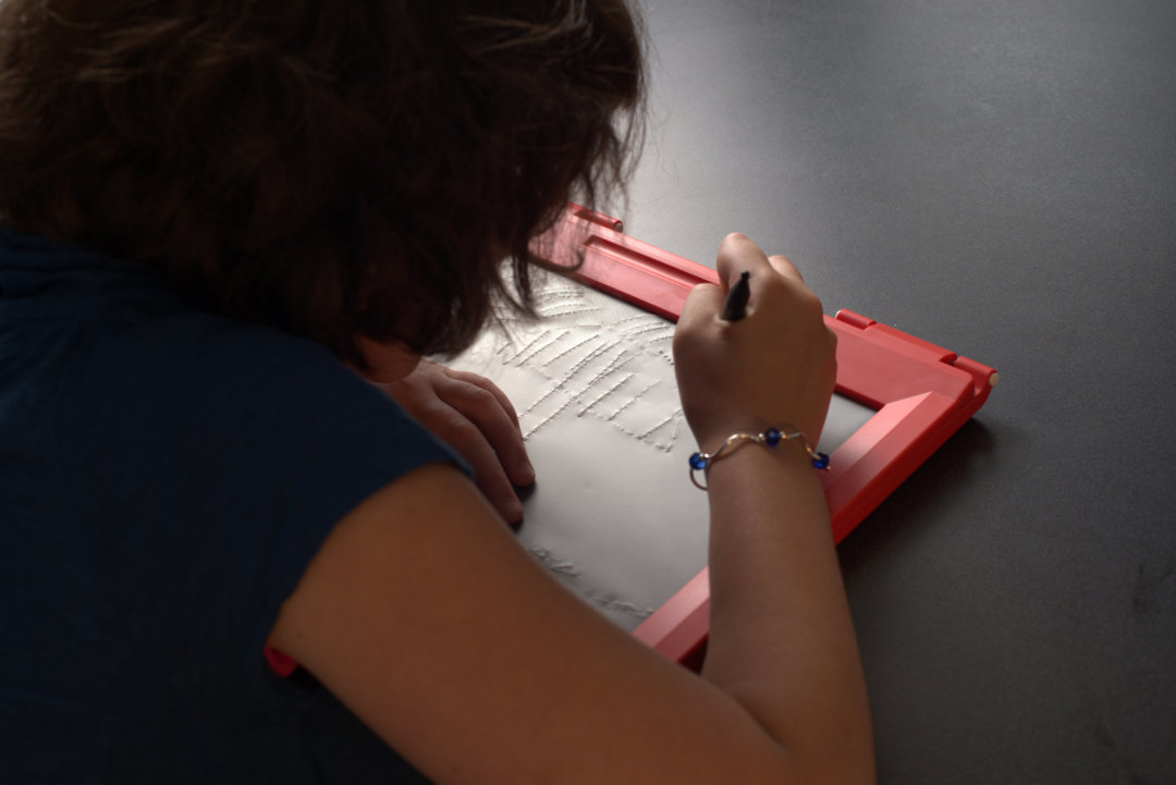 A young girl making tactile graphics on a red intact sketchpad